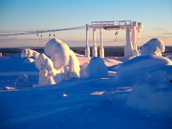 Tief verschneit strecken sich unter diesen bizarren Schneeskulpturen zähe Bäume der Abendsonne in Lappland entgegen.